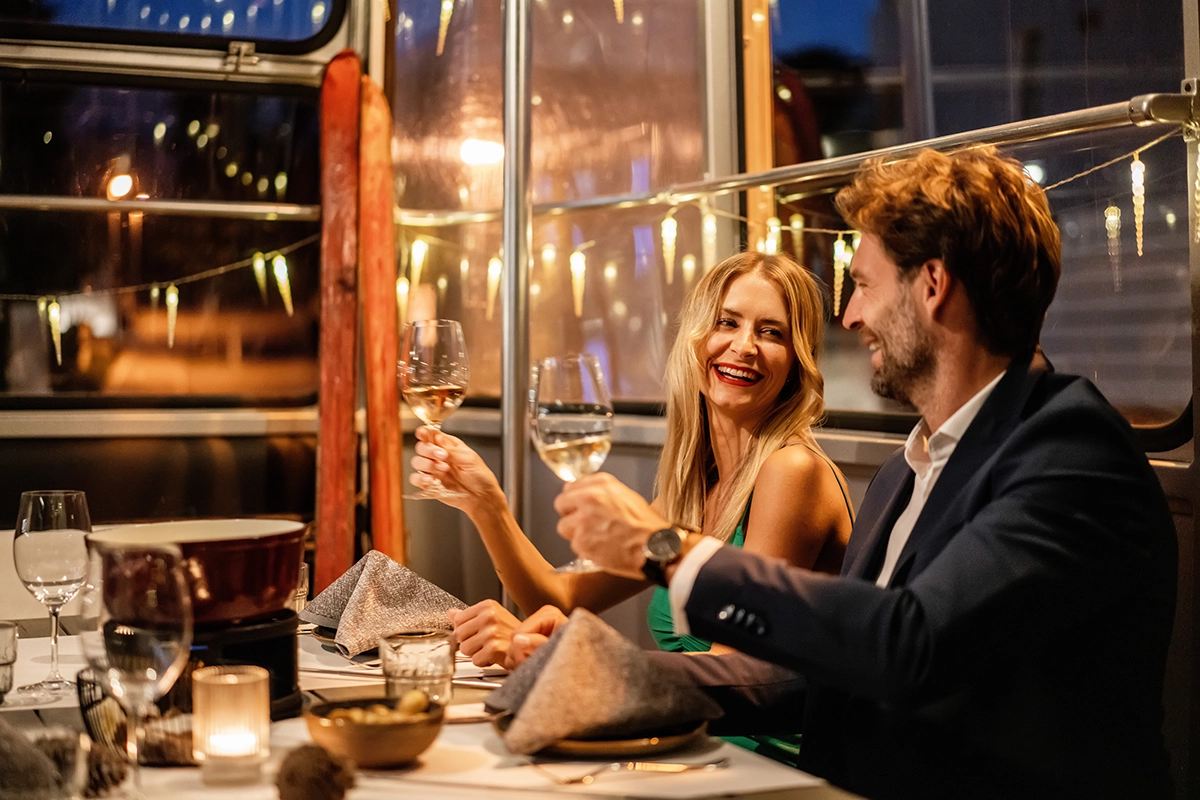 Eine Frau und ein Mann sitzen in der Fonduegondel und stossen mit ihrem Glas Weisswein an
